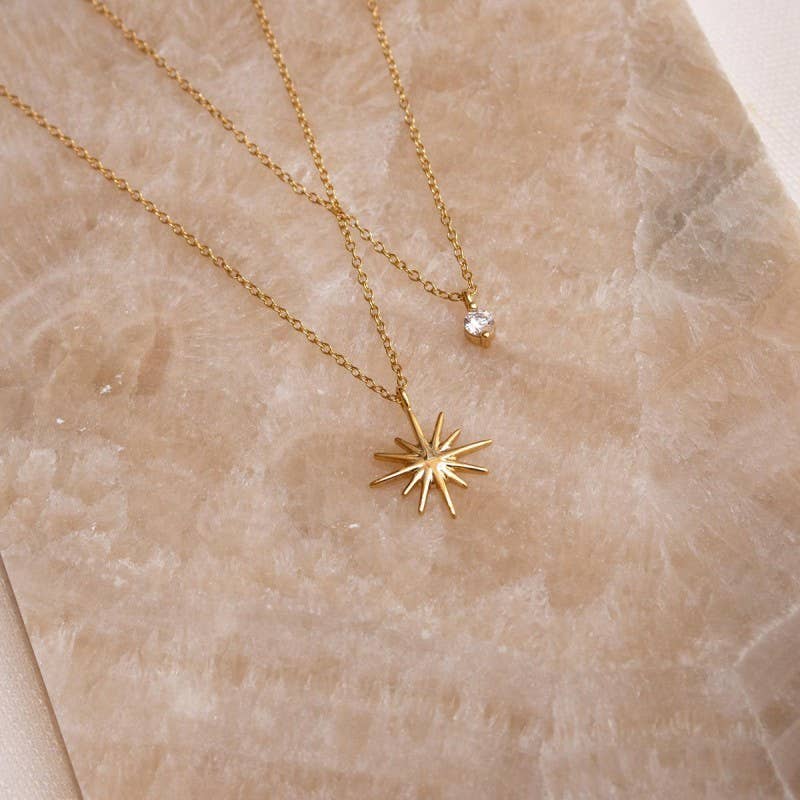 Gold necklace with a star-shaped pendant and a CZ stone on a beige marble surface.
