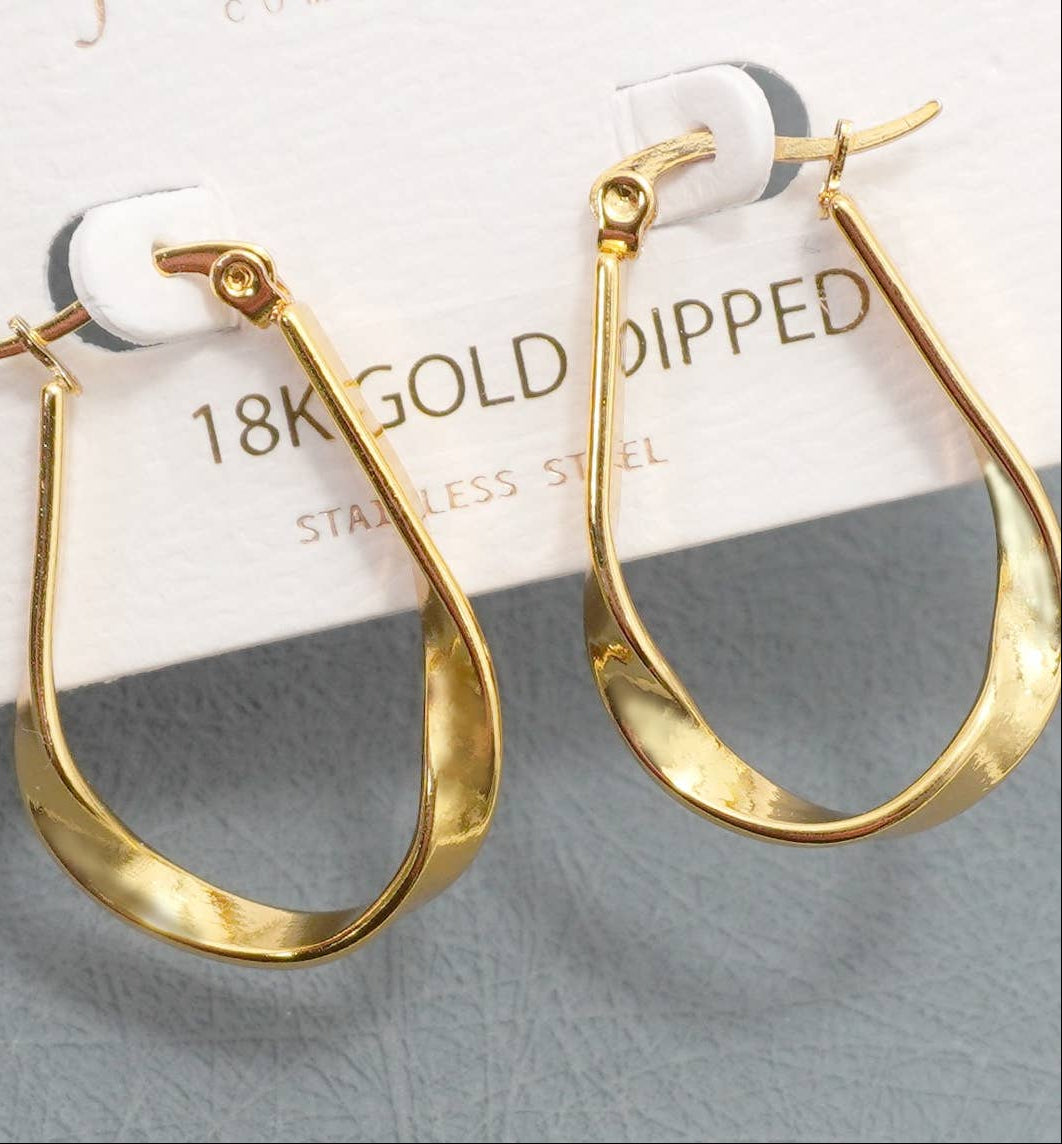 A pair of gold-dipped twist-shaped hoop earrings on a white display card labeled '18K GOLD DIPPED' and 'STAINLESS STEEL', set against a textured gray background.
