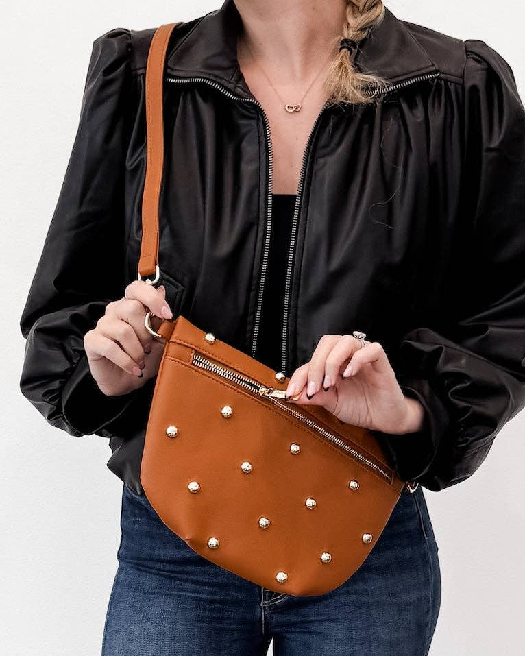 Person holding a brown leather bag with gold studs against a white background.