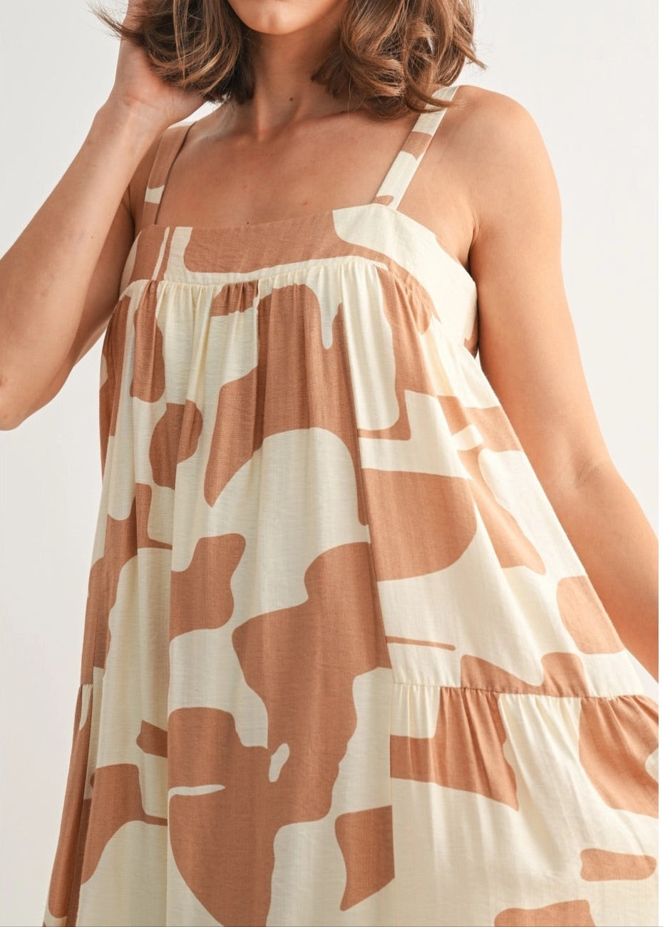 Woman wearing a flowy midi-length dress with wide straps in a cream and terracotta abstract print.