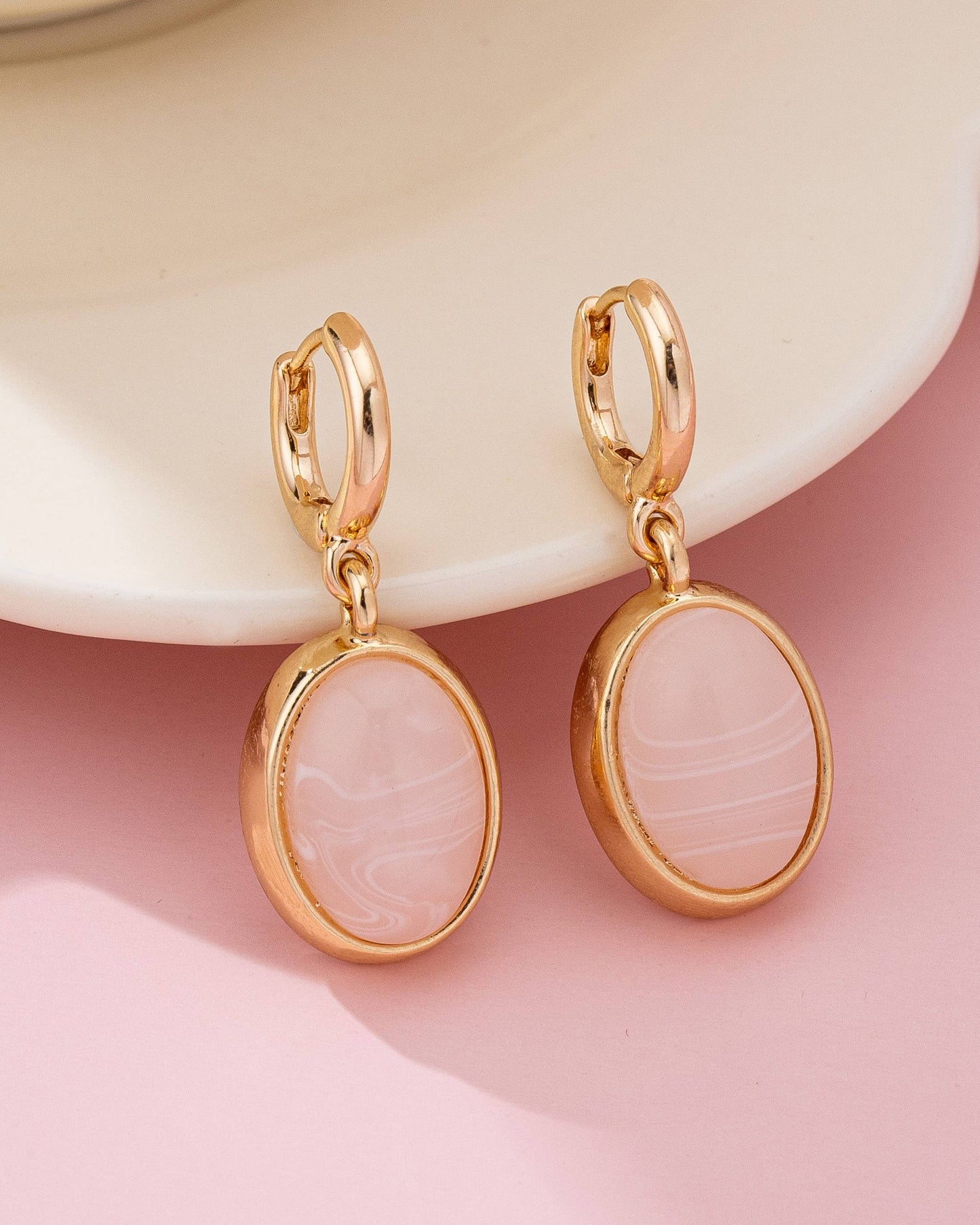 Gold earrings with creamy pink stones on a pink background