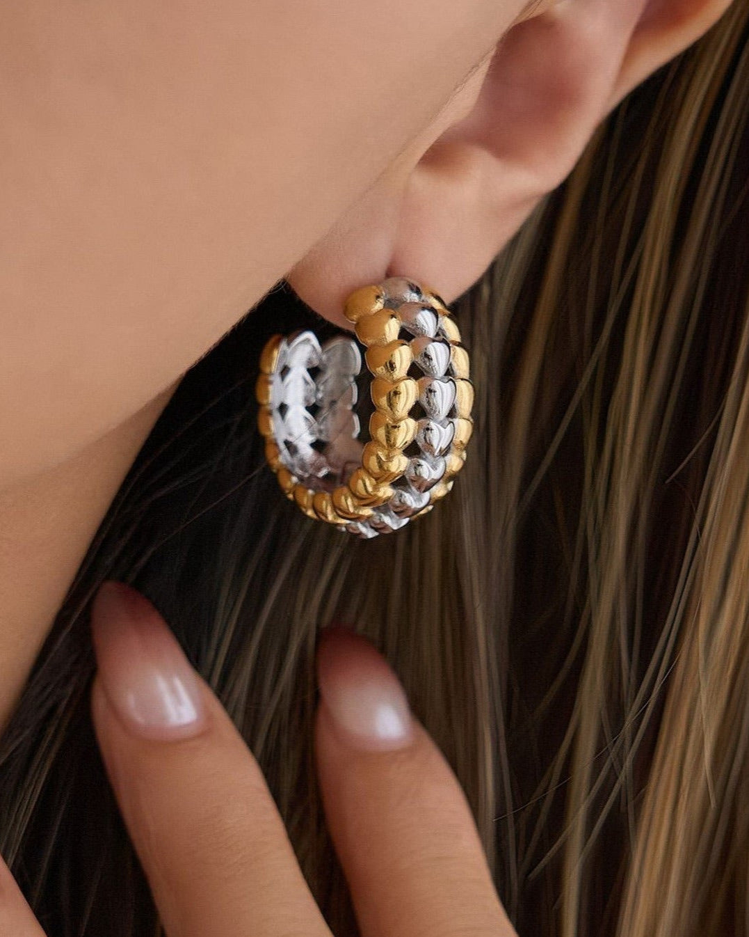 Close-up of a person wearing a gold and silver heart hoop earring.