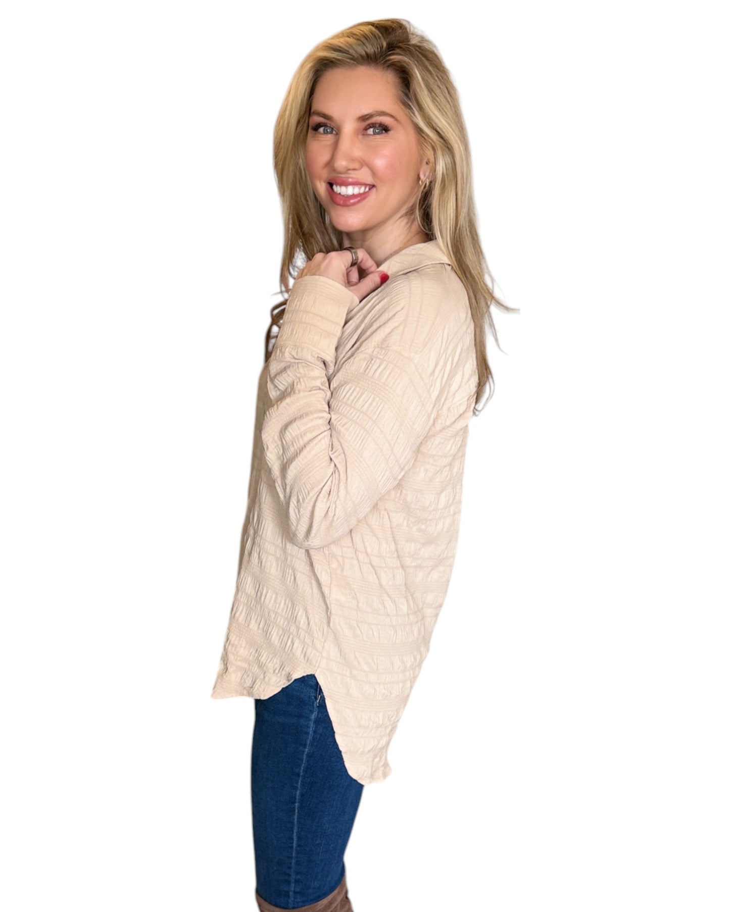 Blonde woman smiling while wearing the Almond Button Down Shirt paired with blue jeans. The shirt features a textured fabric, long sleeves, and a relaxed fit with a curved hem.
