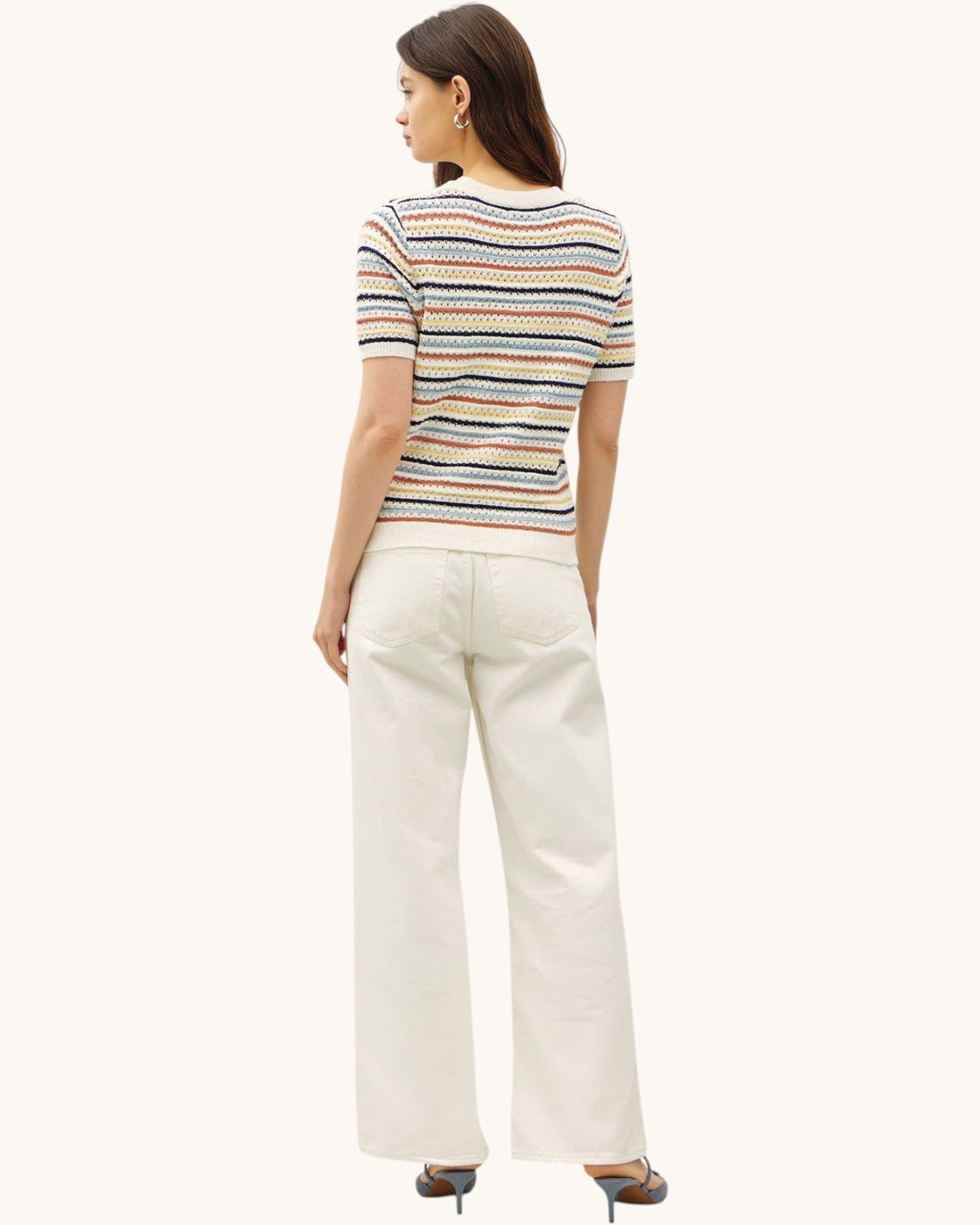 A woman shown from the back wearing a short-sleeve knit top with thin multicolor horizontal stripes and off-white wide-leg trousers, photographed against a plain light background.