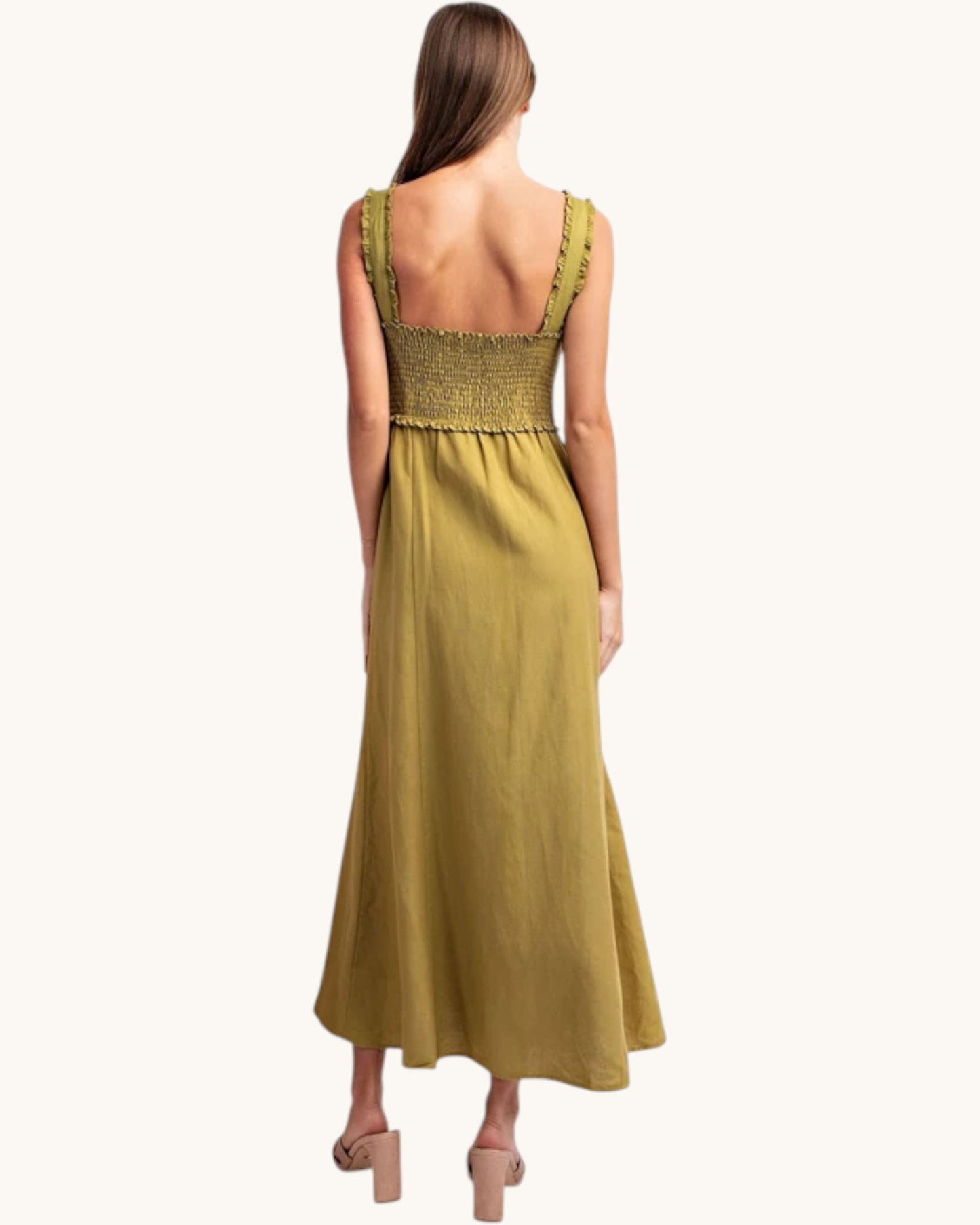 A woman shown from the back wearing a sleeveless olive green maxi dress with a smocked bodice and ruffled straps, paired with beige block-heel sandals, against a plain off-white background.
