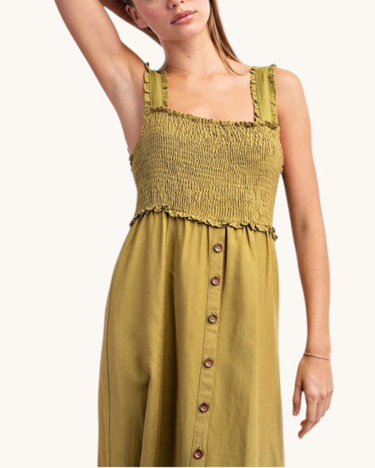 A woman wearing a sleeveless olive green dress with a smocked bodice, ruffled straps, and a button-front skirt, shown against a plain light background.