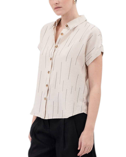 Person wearing a light khaki short-sleeve button up shirt with brown buttons and black pants on a white background.