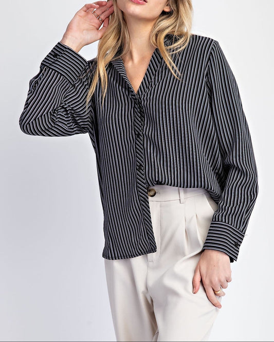 Woman wearing a black and white striped shirt with white pants on a light gray background.