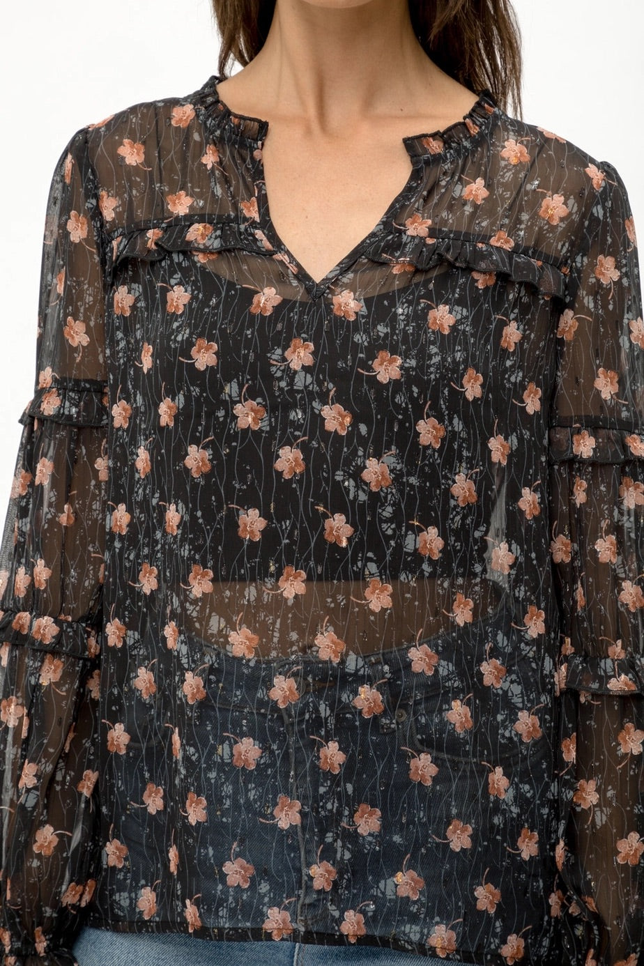 Woman wearing a black semi-sheer floral blouse with a white background.