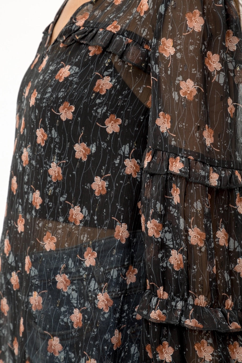 Woman wearing a black semi-sheer floral blouse with a white background.
