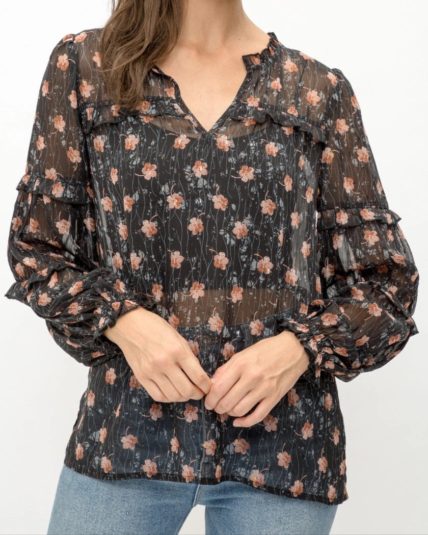 Woman wearing a black semi-sheer floral blouse with a white background.