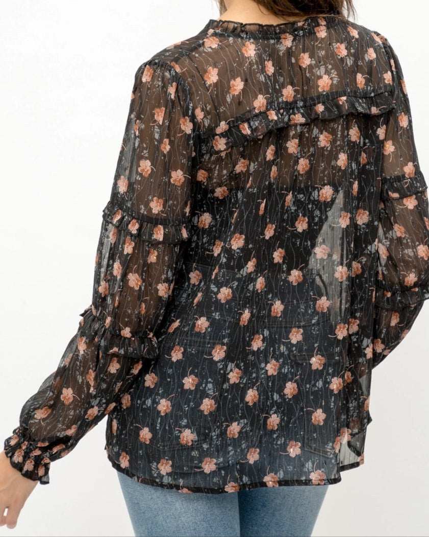 Woman wearing a black semi-sheer floral blouse with a white background.