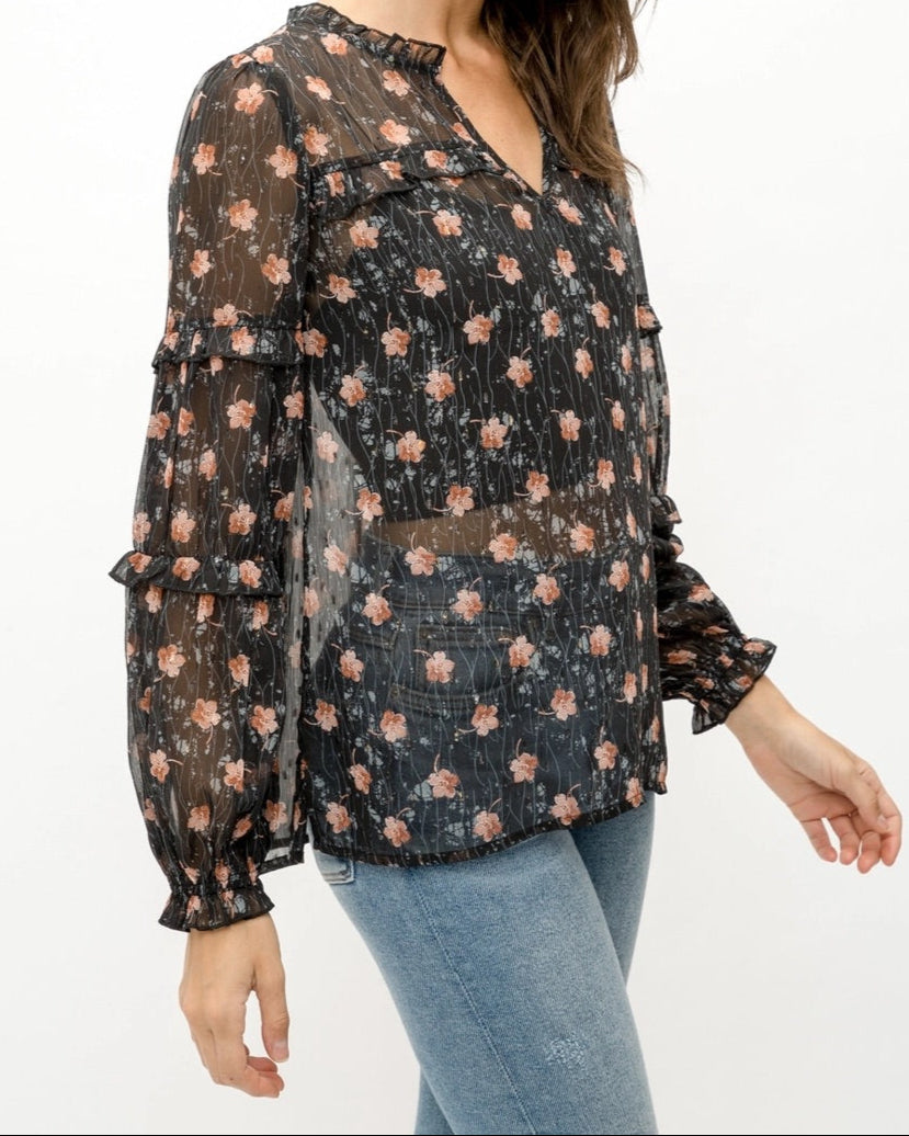 Woman wearing a black semi-sheer floral blouse with a white background.
