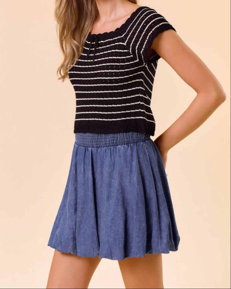 Woman wearing a black and tan striped top and blue denim skirt on a beige background.