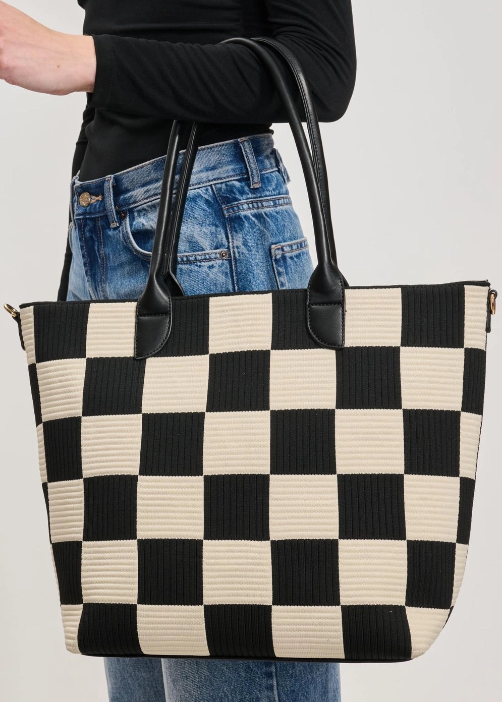 Person holding a black and white checkered tote bag against a plain background.