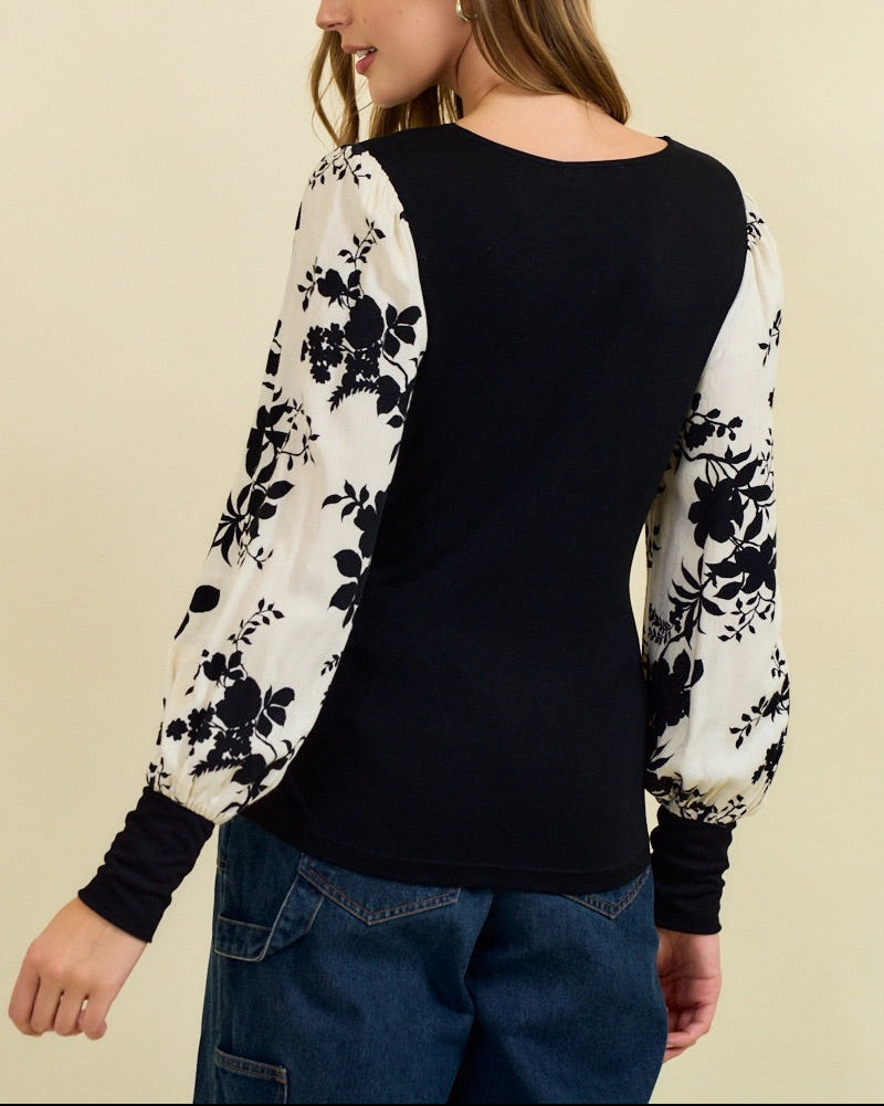 Woman wearing a black top with floral sleeves against a beige background.