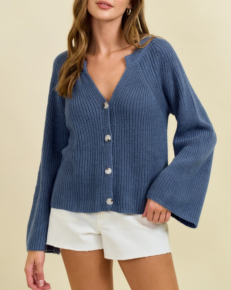 Woman wearing a blue ribbed cardigan over white shorts on a beige background