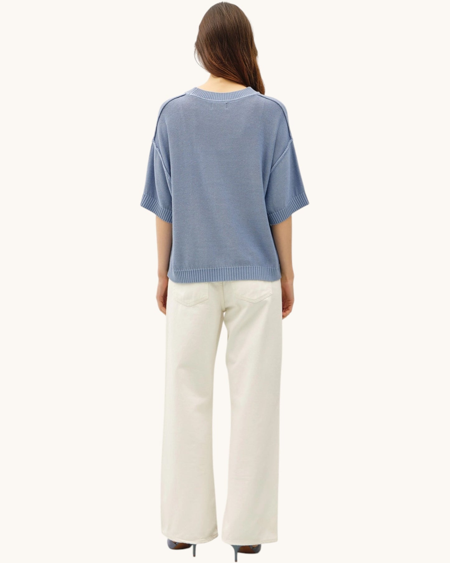 Back view of a person wearing a blue sweater and white pants on a white background.