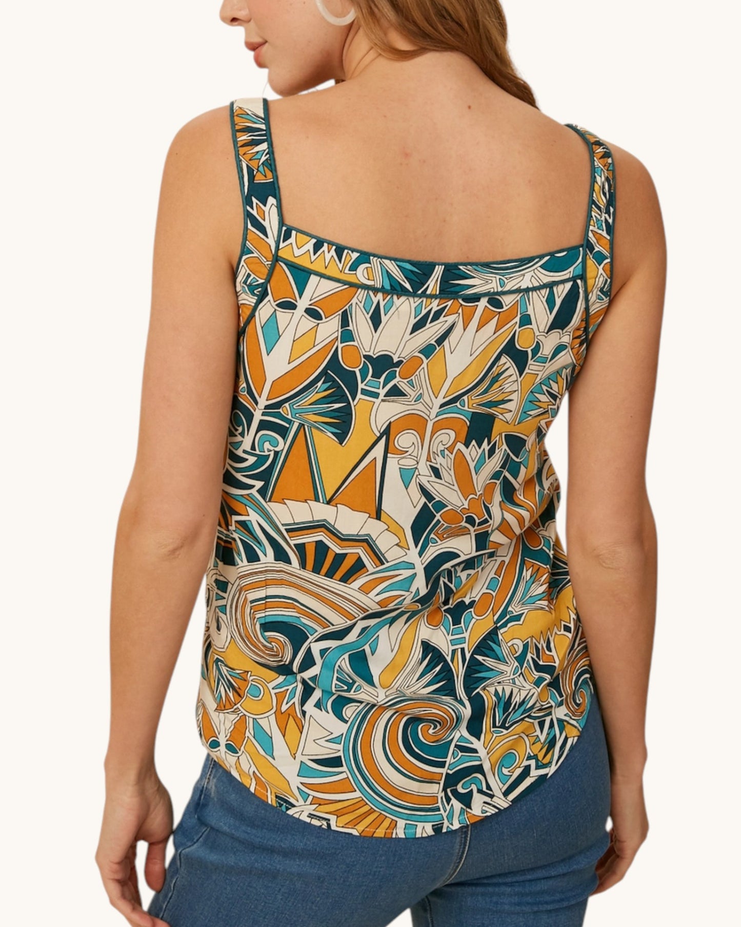 Woman wearing a patterned boho top and blue jeans on a white background.