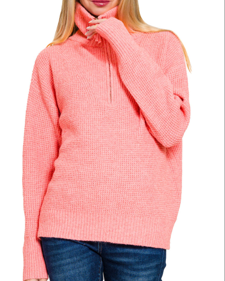Woman wearing a bright peachy pink pullover sweater with a white background.