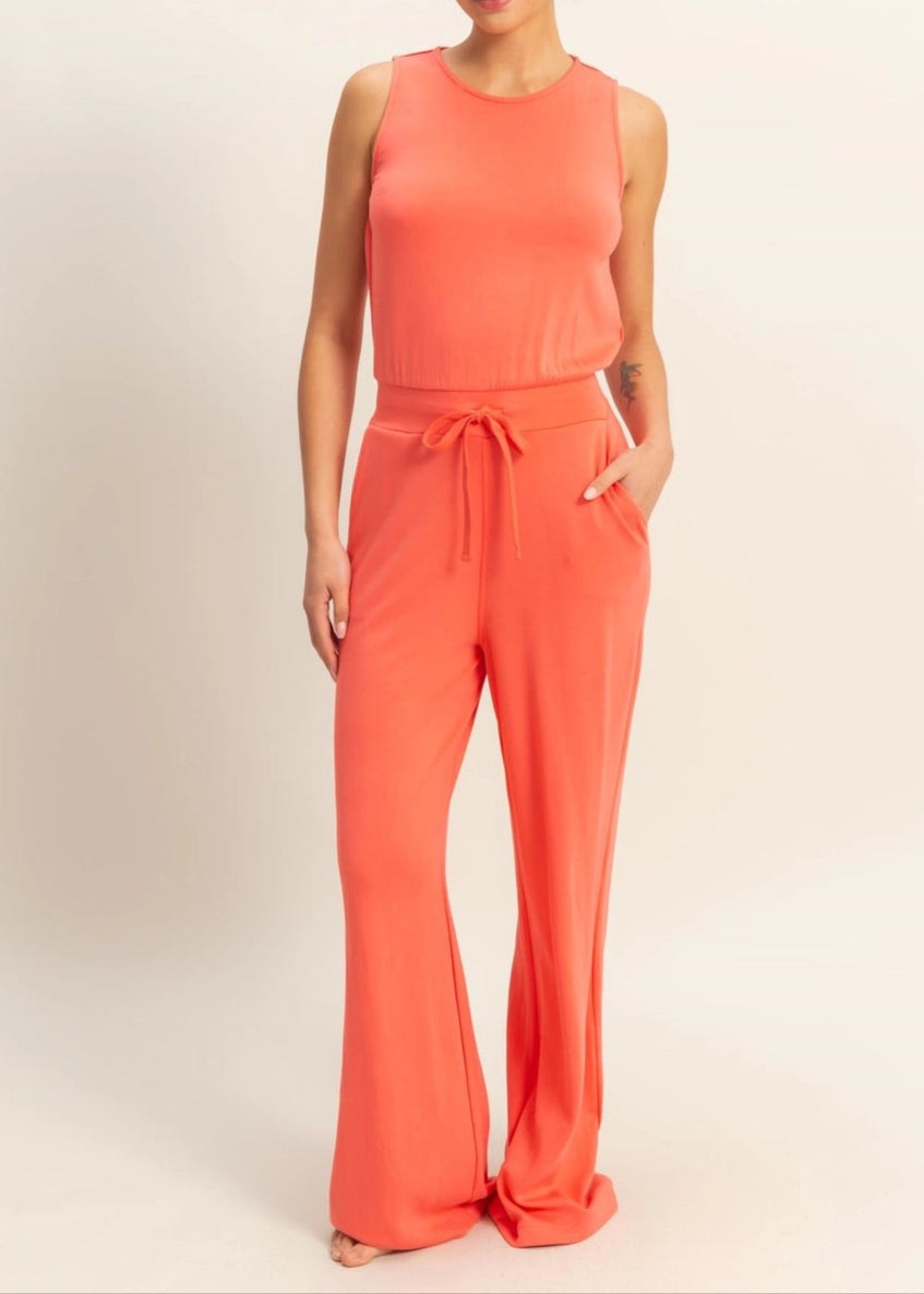 Woman wearing Sunset Hour Sleeveless Jumpsuit in Coral with cinched waist and high scoop neckline.