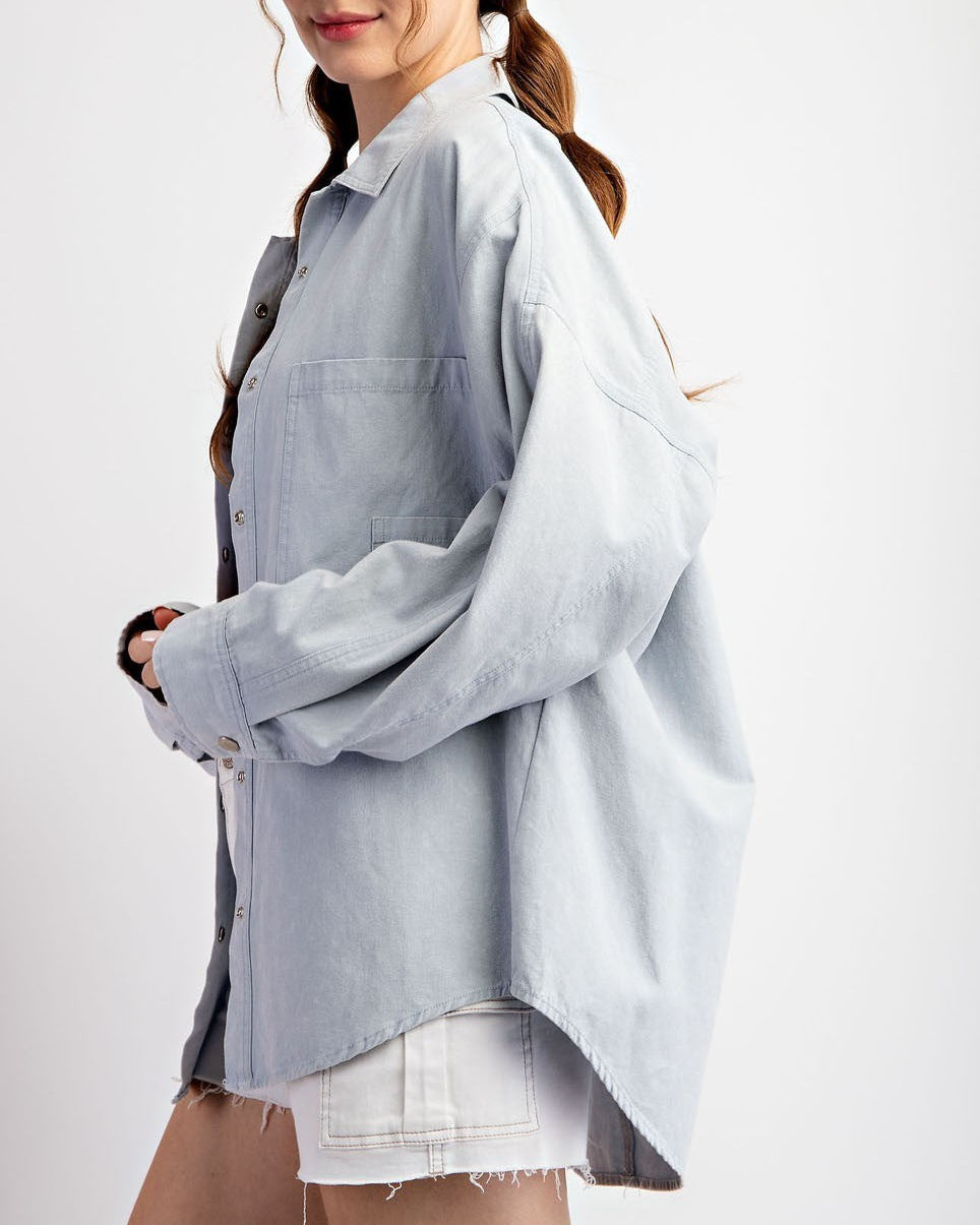 Woman wearing a light blue denim shirt jacket / shacket over a white top on a white background.