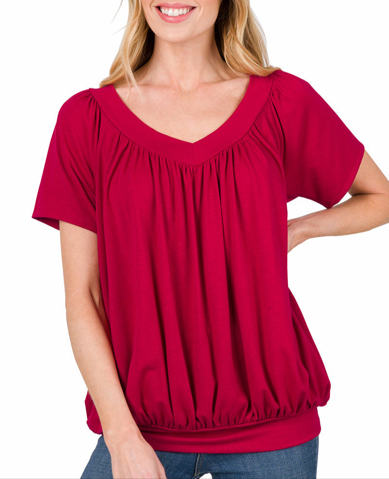 Woman wearing a burgundy short sleeve top with banded hem with jeans on a white background.