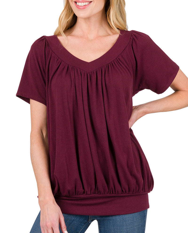 Woman wearing a burgundy short sleeve top with banded hem with jeans on a white background.
