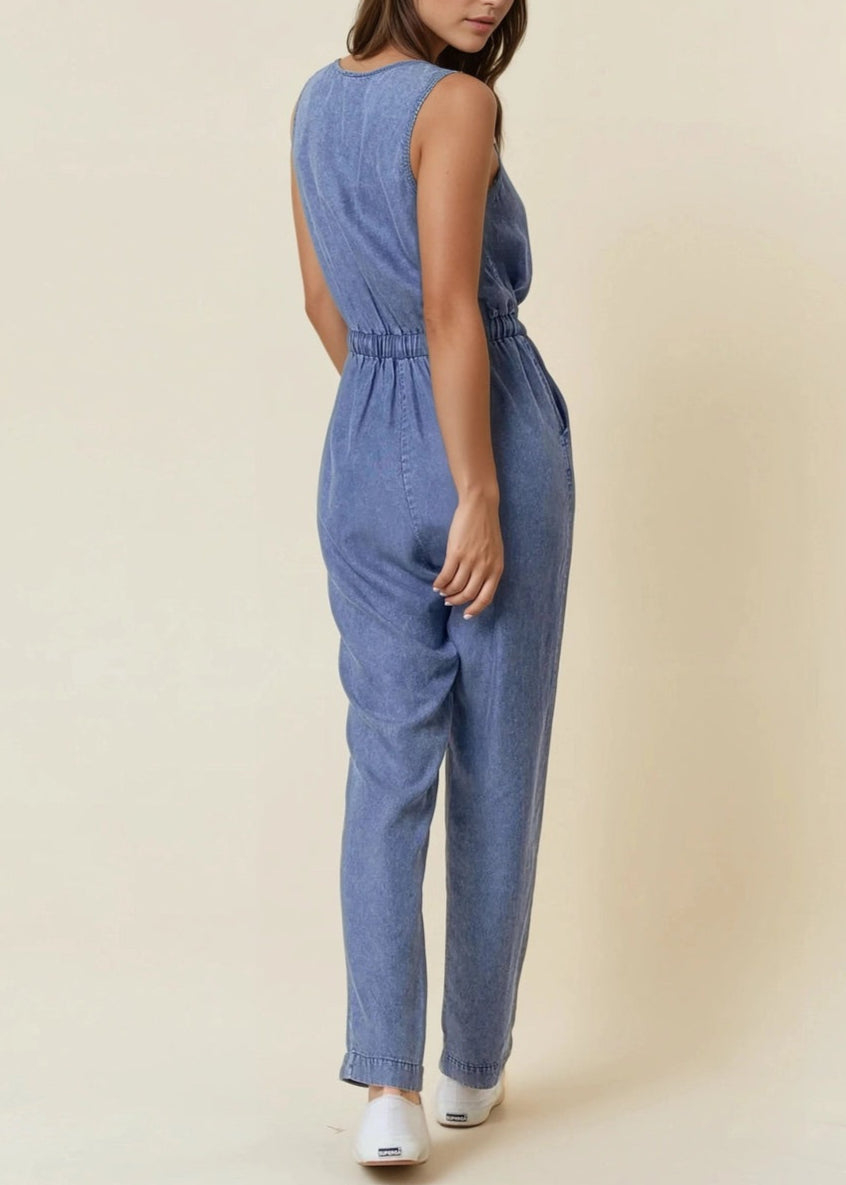 Sleeveless medium wash denim jumpsuit with scoop neck and drawstring waist.
