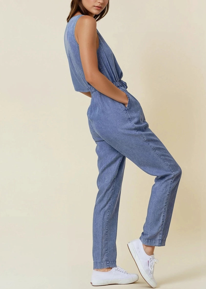 Sleeveless medium wash denim jumpsuit with scoop neck and drawstring waist.