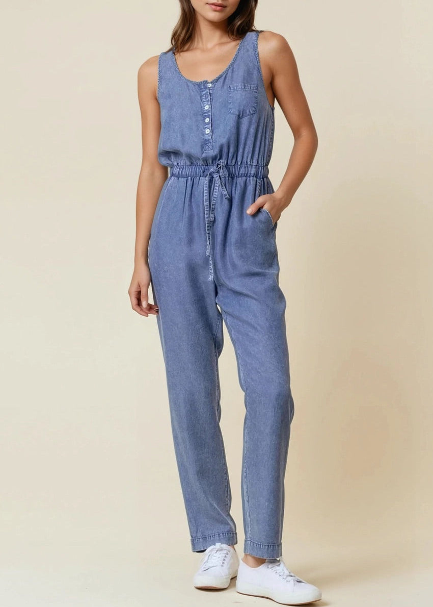Sleeveless medium wash denim jumpsuit with scoop neck and drawstring waist.