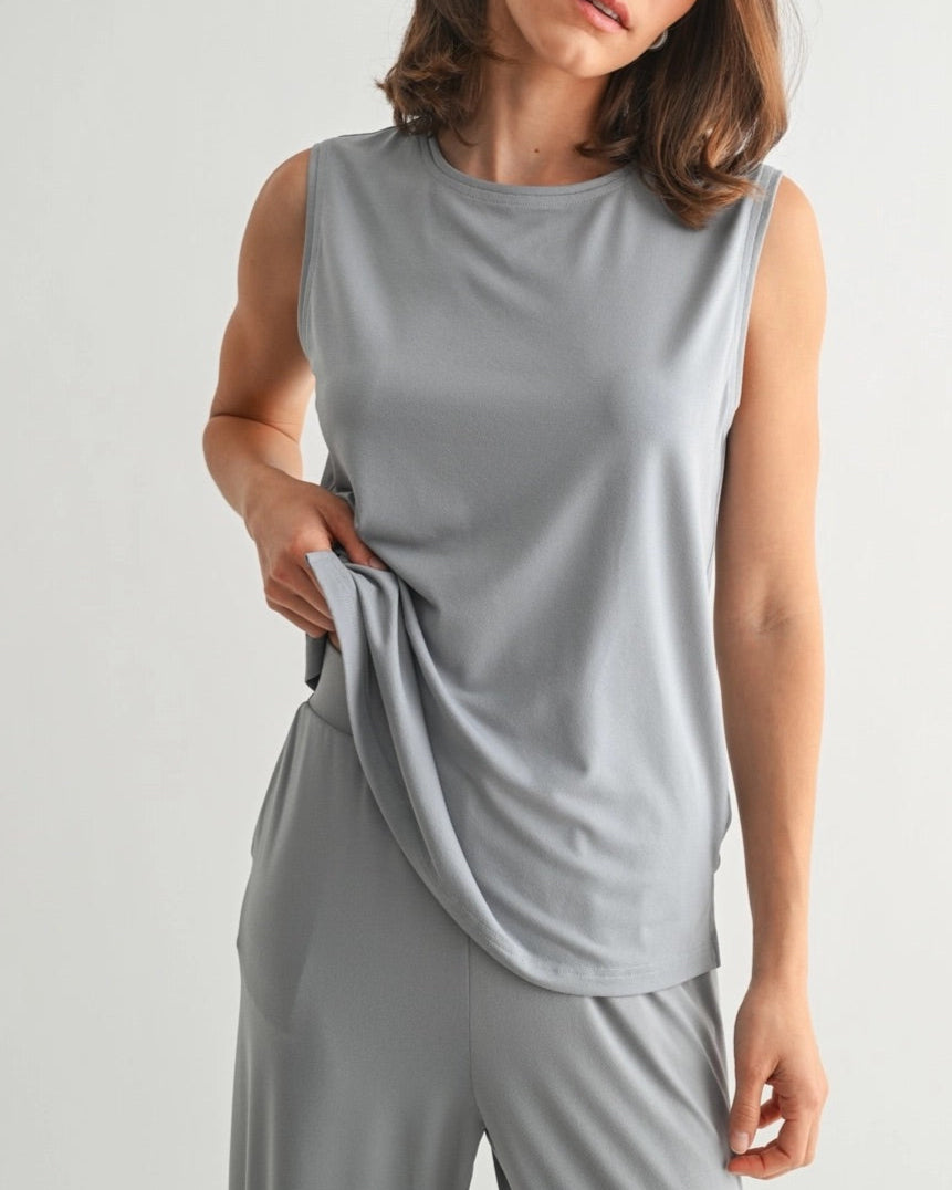 Woman wearing a dusty blue sleeveless lounge tank with relaxed drape and soft stretch.