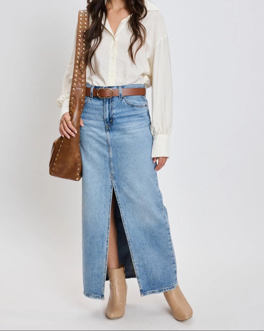 Woman wearing a white blouse, blue jeans, and beige boots with a brown handbag on a white background.