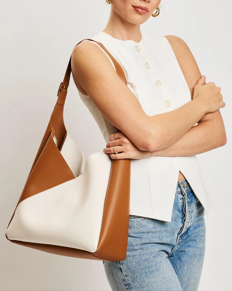 Woman holding a brown and white handbag against a plain background