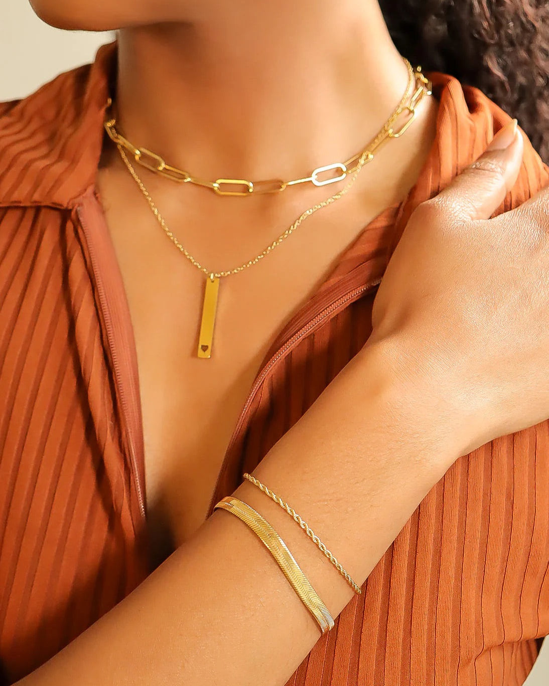 Person wearing gold necklaces and bracelet on a neutral background.