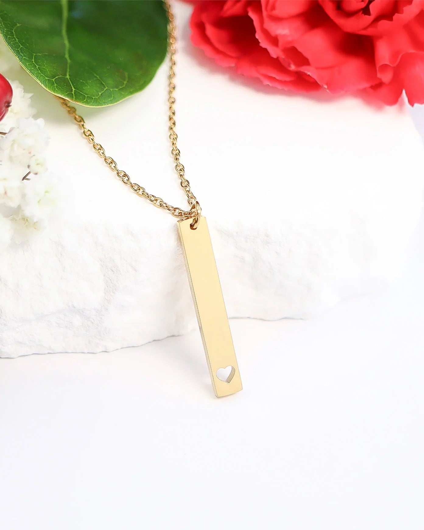 Gold necklace with a heart-shaped pendant on a white surface with red flowers in the background