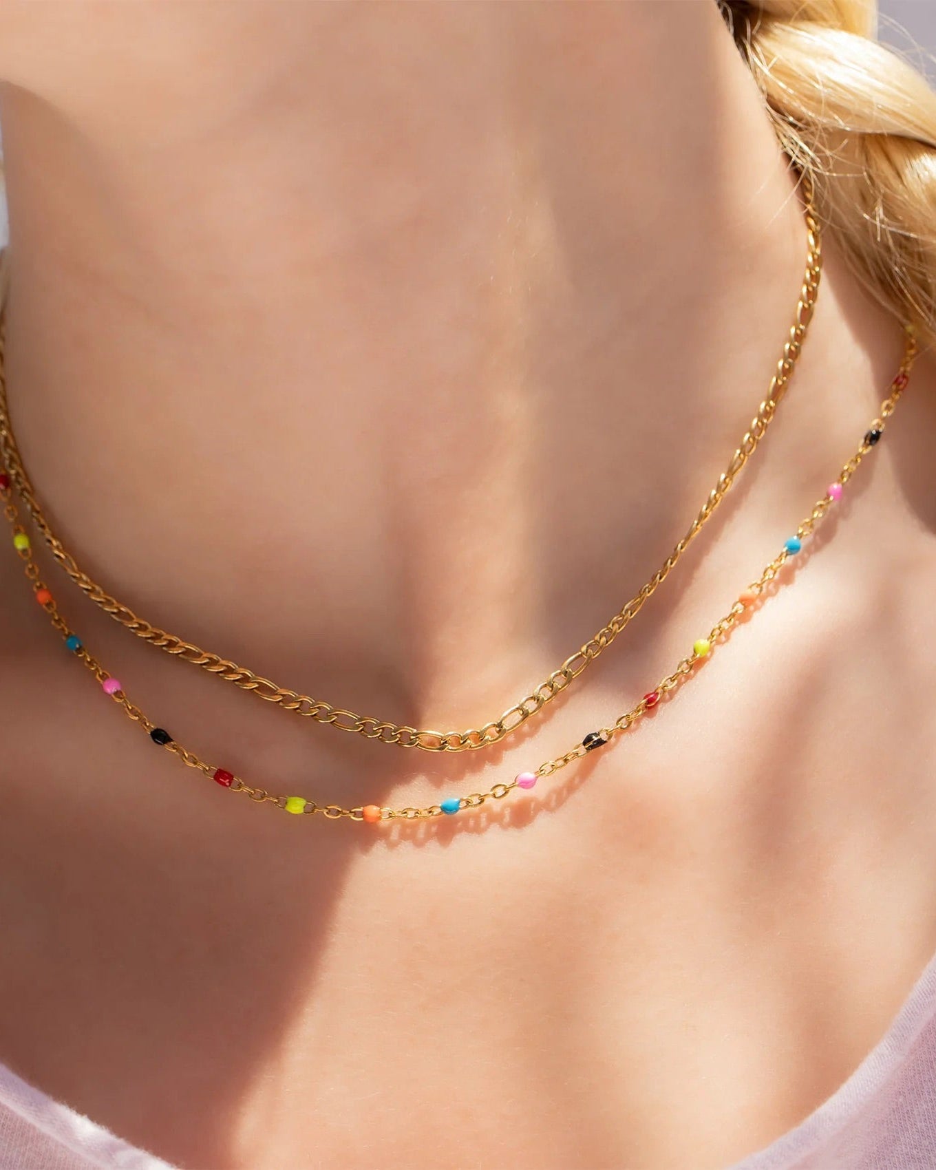 Gold necklace with colorful beads worn by a person with a blurred background.