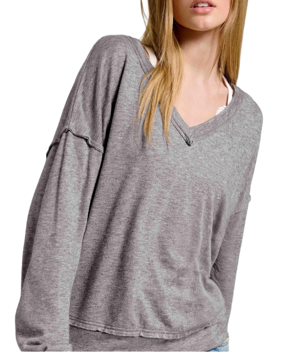 Woman wearing a gray oversized long sleeve top with raw edge trim on a white background.