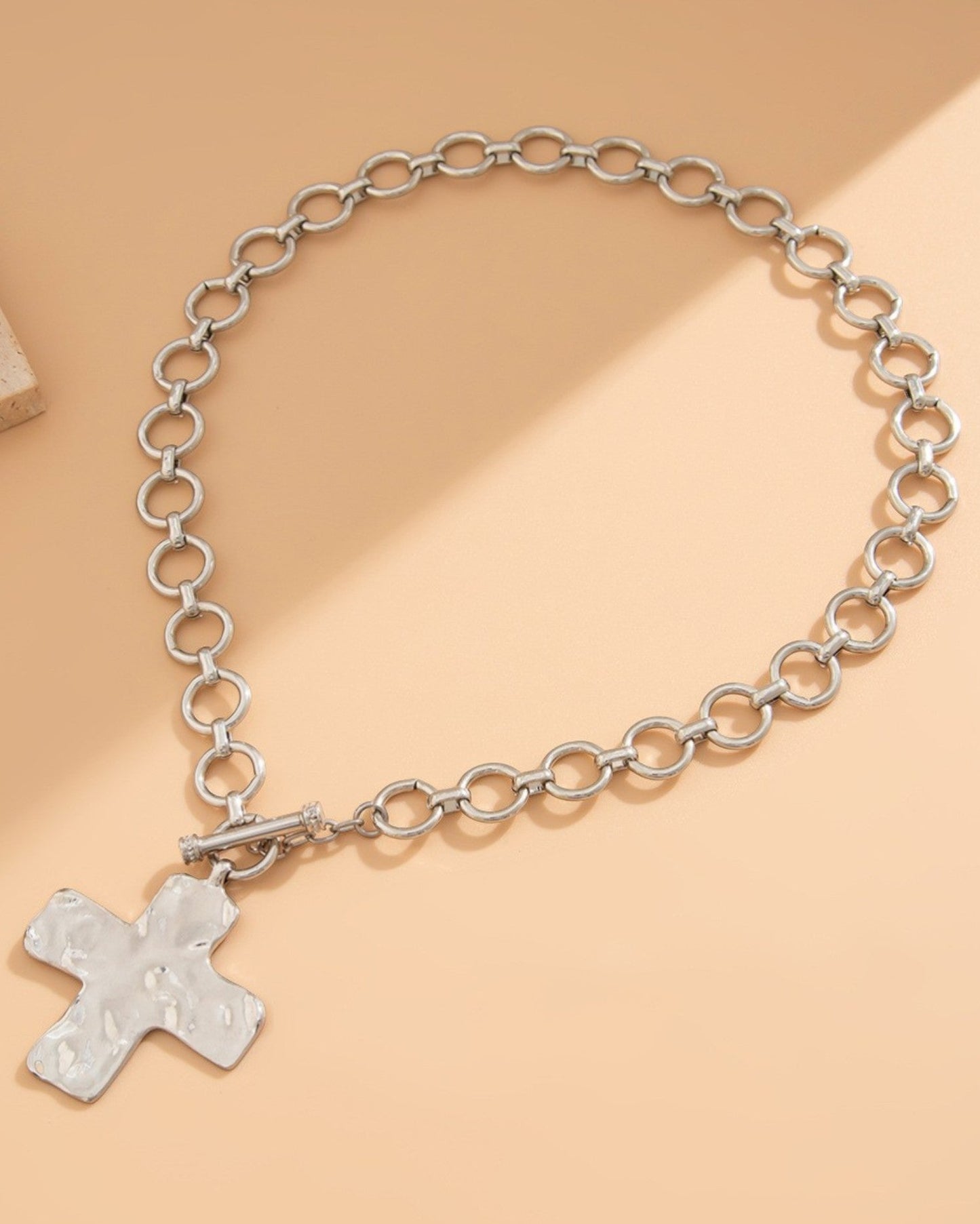 Silver chain necklace with a large cross pendant on a beige background.