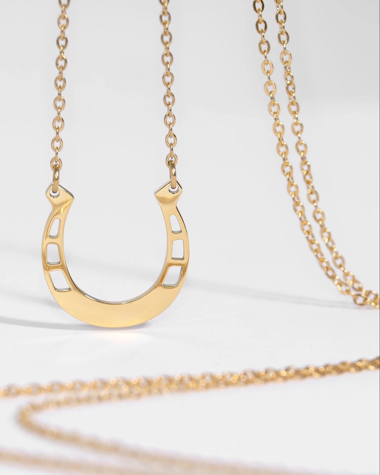 Gold horseshoe-shaped pendant on a gold chain against a white background.