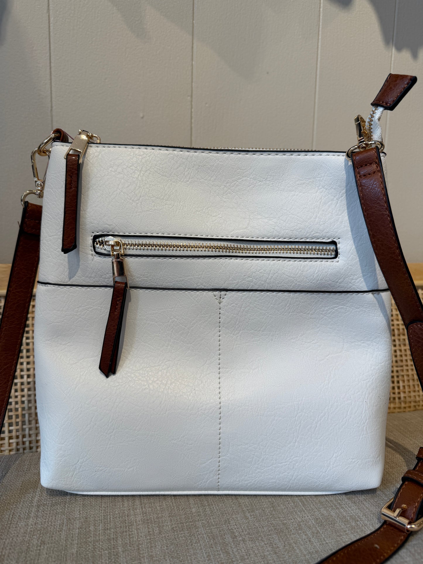 A white pebbled leather crossbody bag with brown leather straps and gold-tone hardware, shown against a neutral indoor background.
