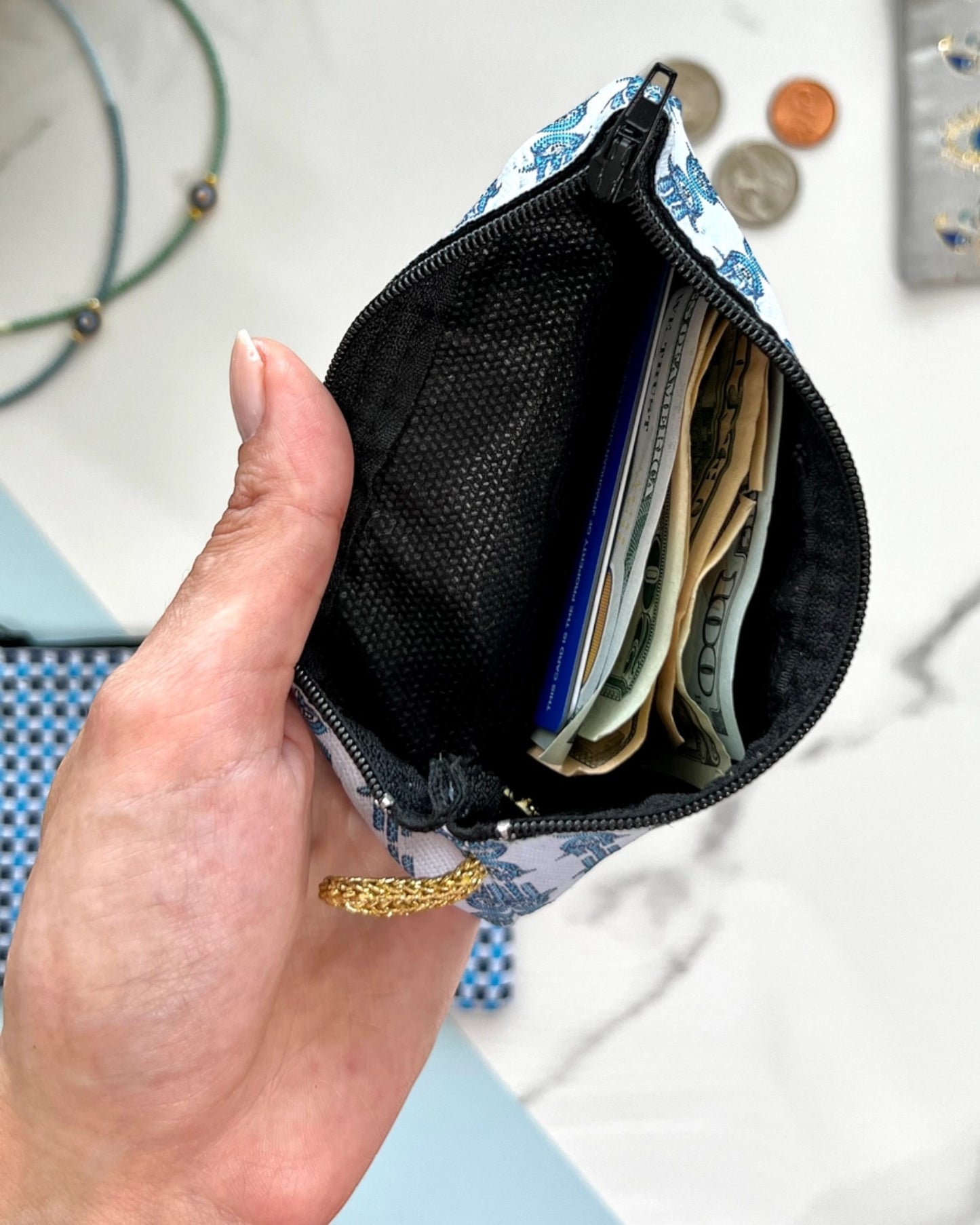 Hand holding a small pouch with black interior containing money and cards against a blurred background.