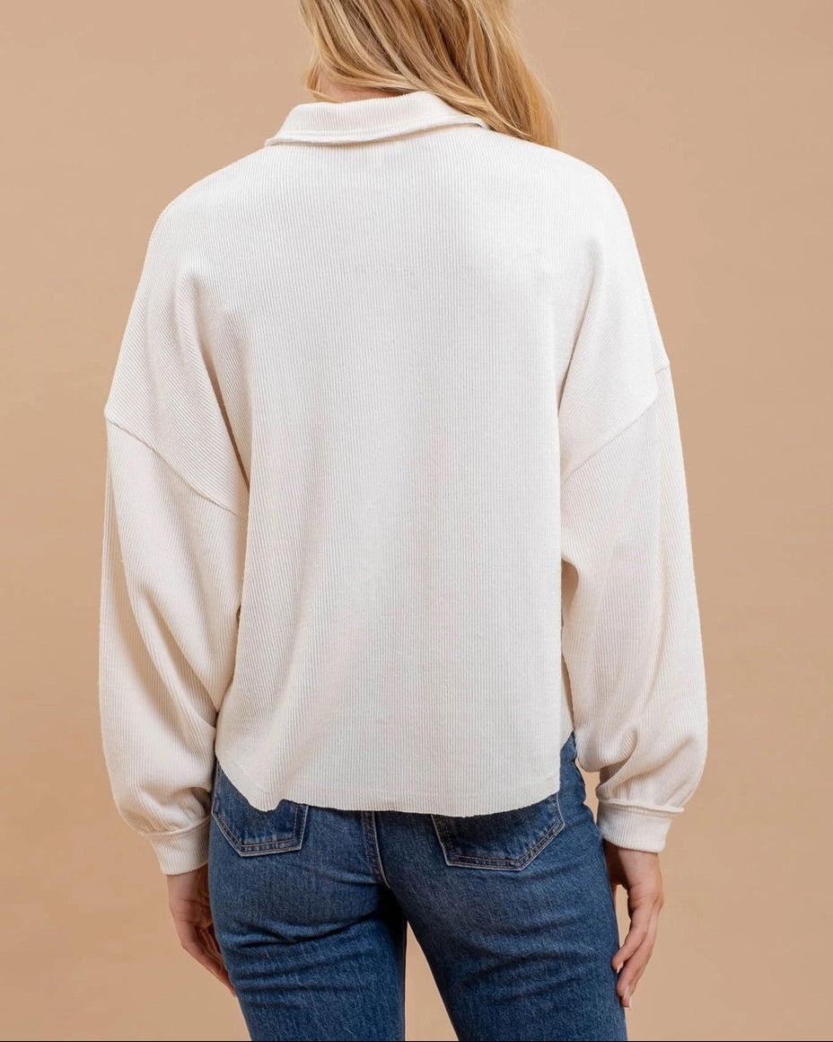 Person wearing a cream-colored sweater and blue jeans against a beige background.