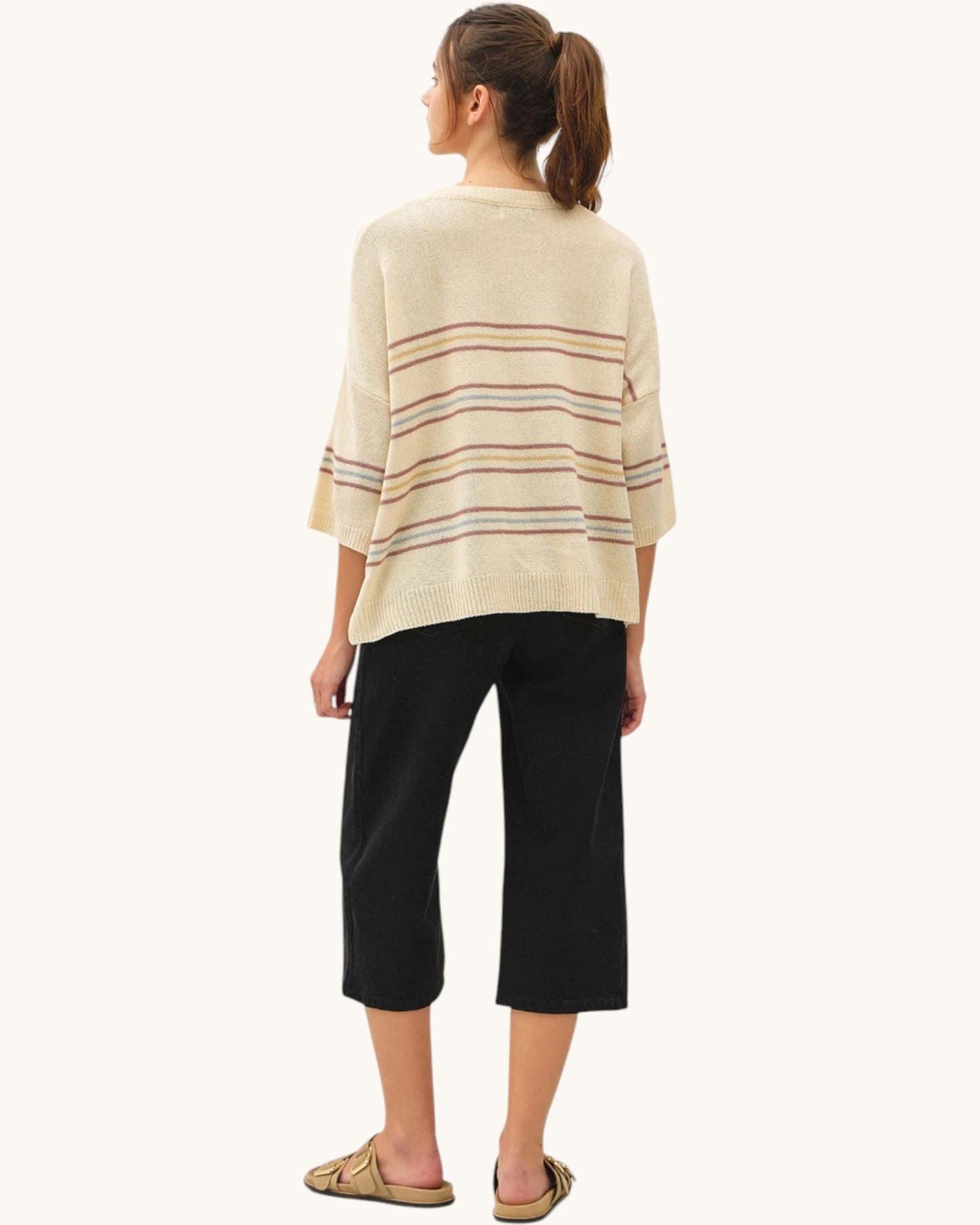 Woman wearing a light beige striped sweater and black pants on a white background.