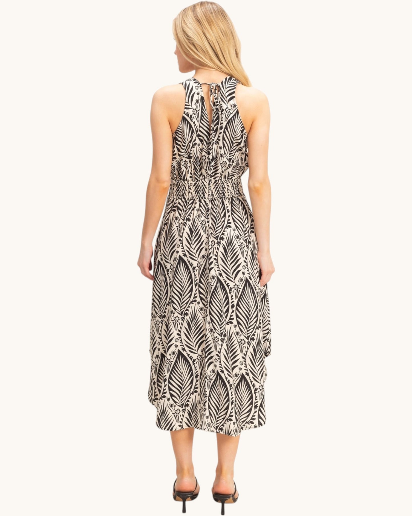 Back view of a woman wearing a tropical patterned beige dress on a white background.