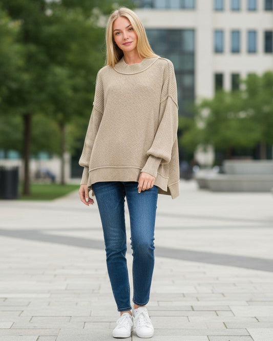 Woman wearing a light mocha sweater and blue jeans standing in an urban setting.