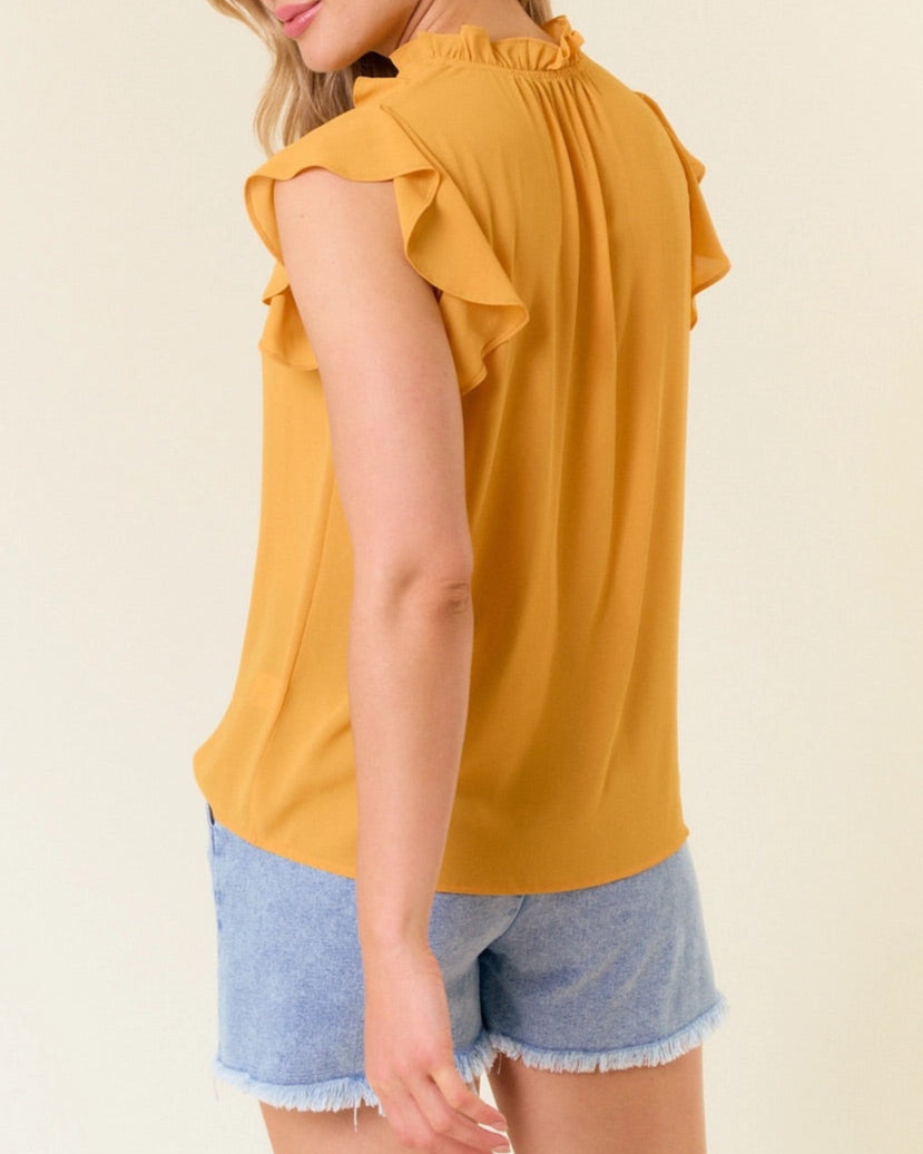 Woman wearing a yellow ruffled top and denim shorts against a plain background.