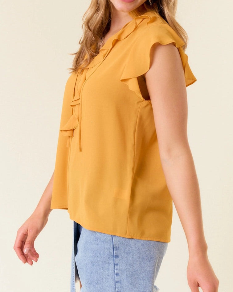 Woman wearing a yellow blouse with ruffles and denim shorts against a plain background.