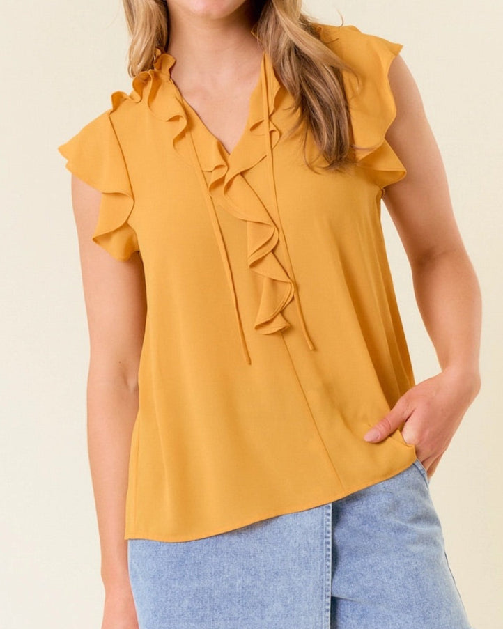 Woman wearing a yellow ruffled top and denim shorts against a plain background.