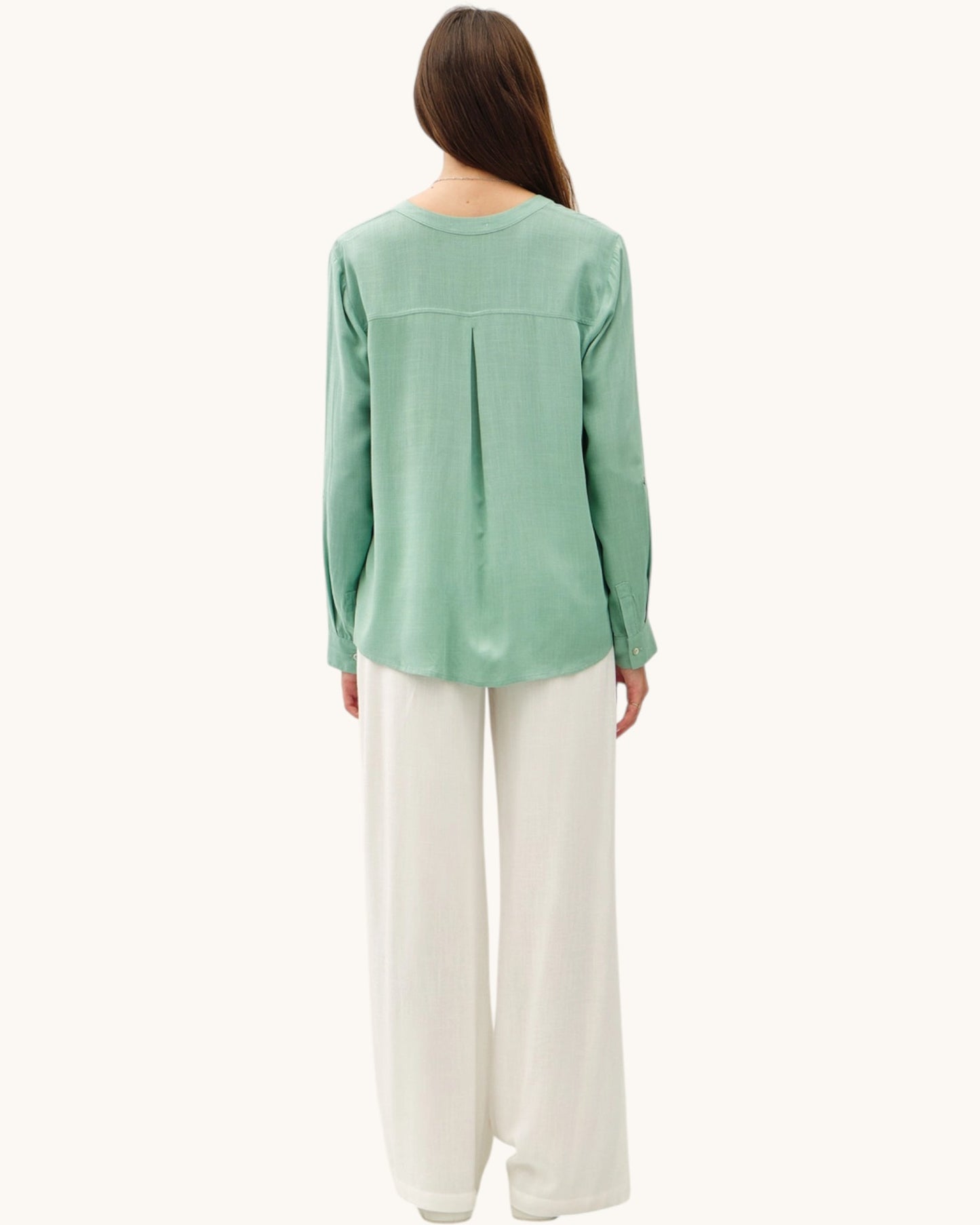 Back view of a person wearing a green long-sleeve top and white pants on a white background.